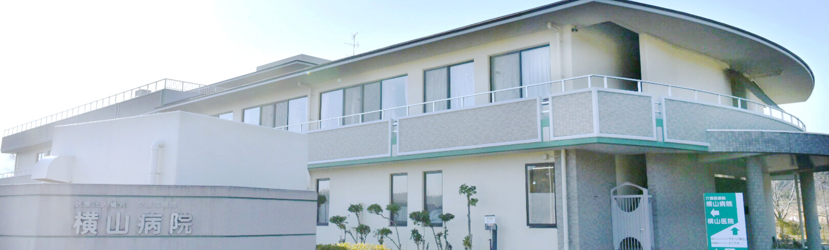 介護施設の建物外観。白基調の2階建て建物で、バルコニーと施設名表示がある。